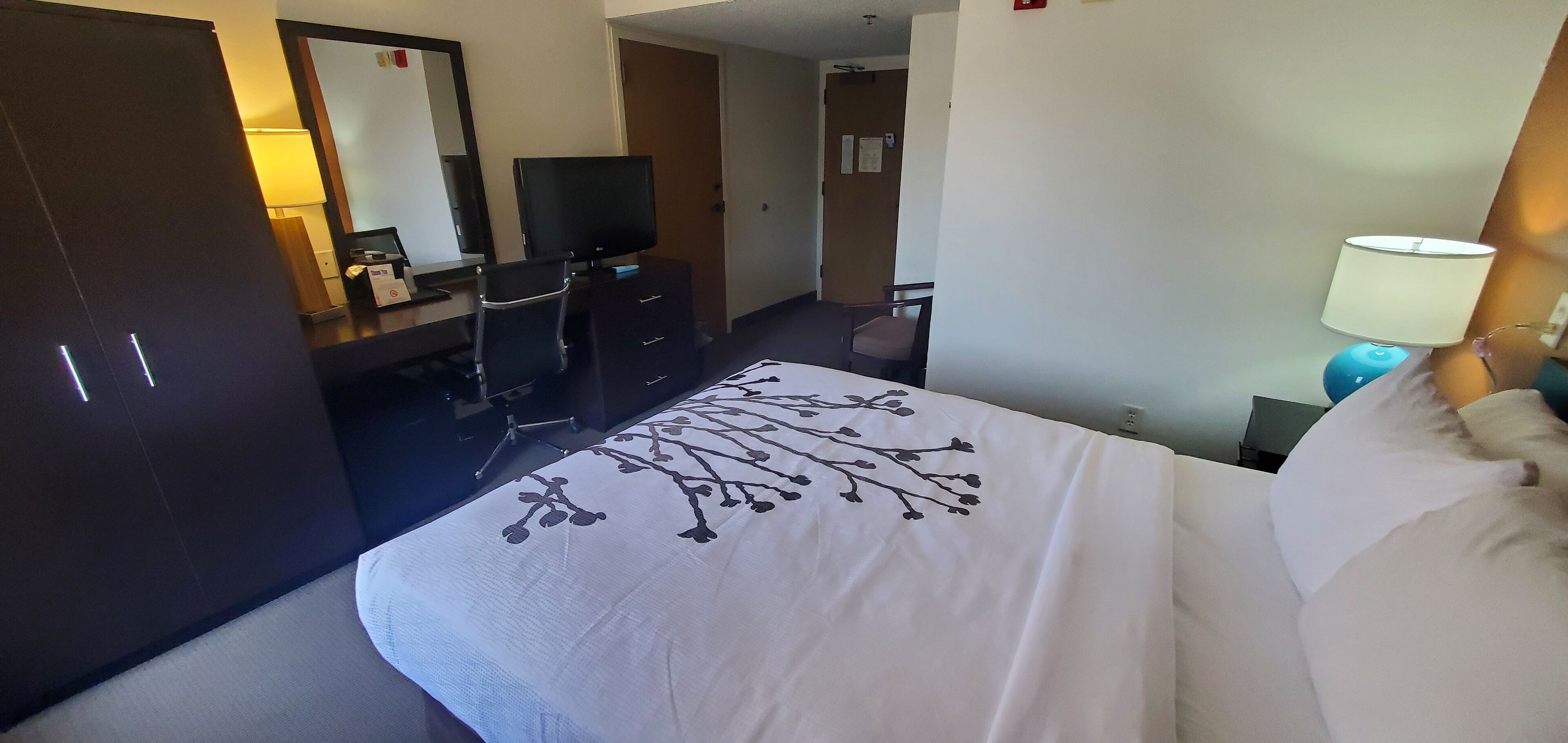 A hotel room with a bed, a desk with a computer, a TV, and a chair.