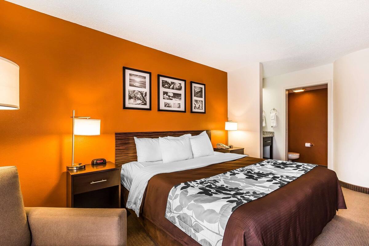 A hotel room with a bed, a nightstand, a lamp, and a chair.