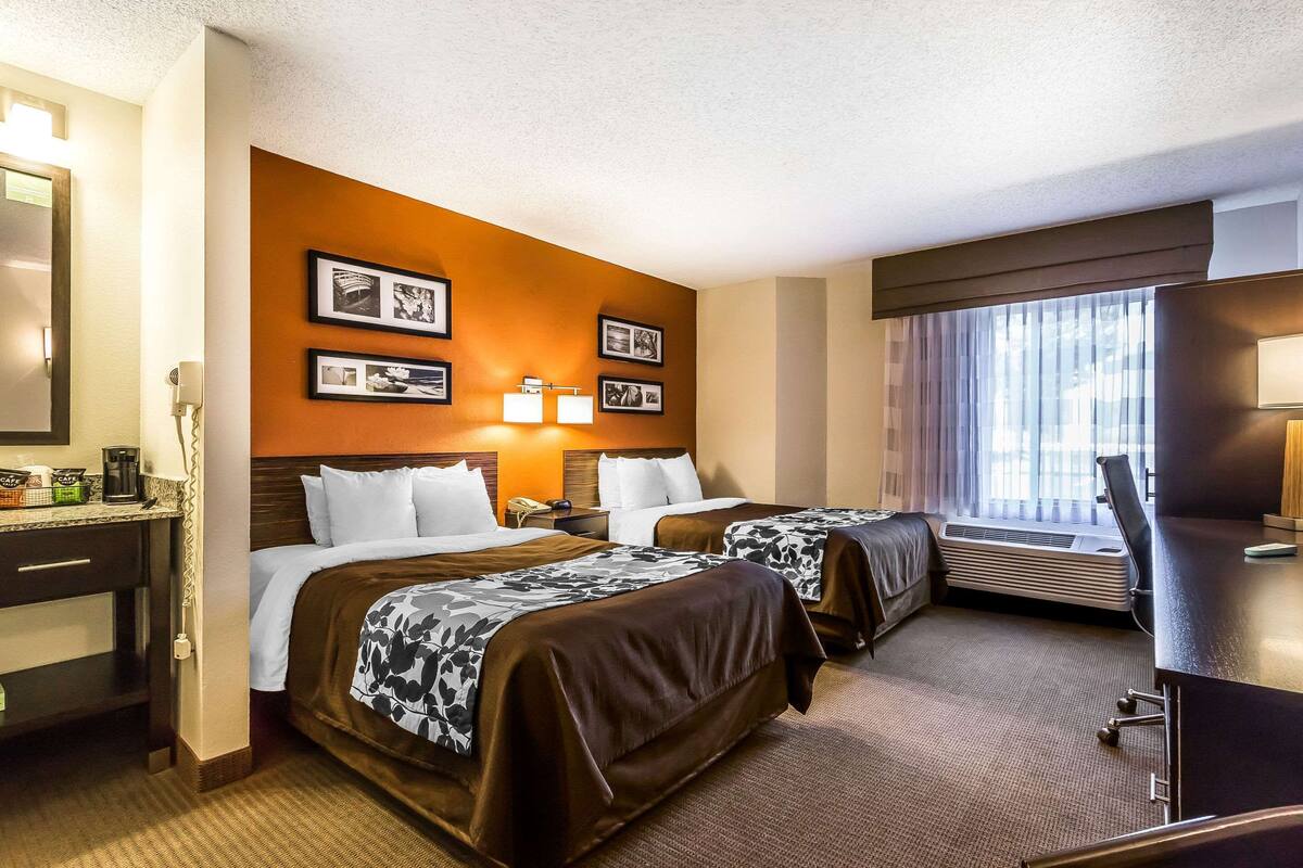A hotel room with two beds, a desk with a coffee maker, a mirror, and framed pictures on the wall.