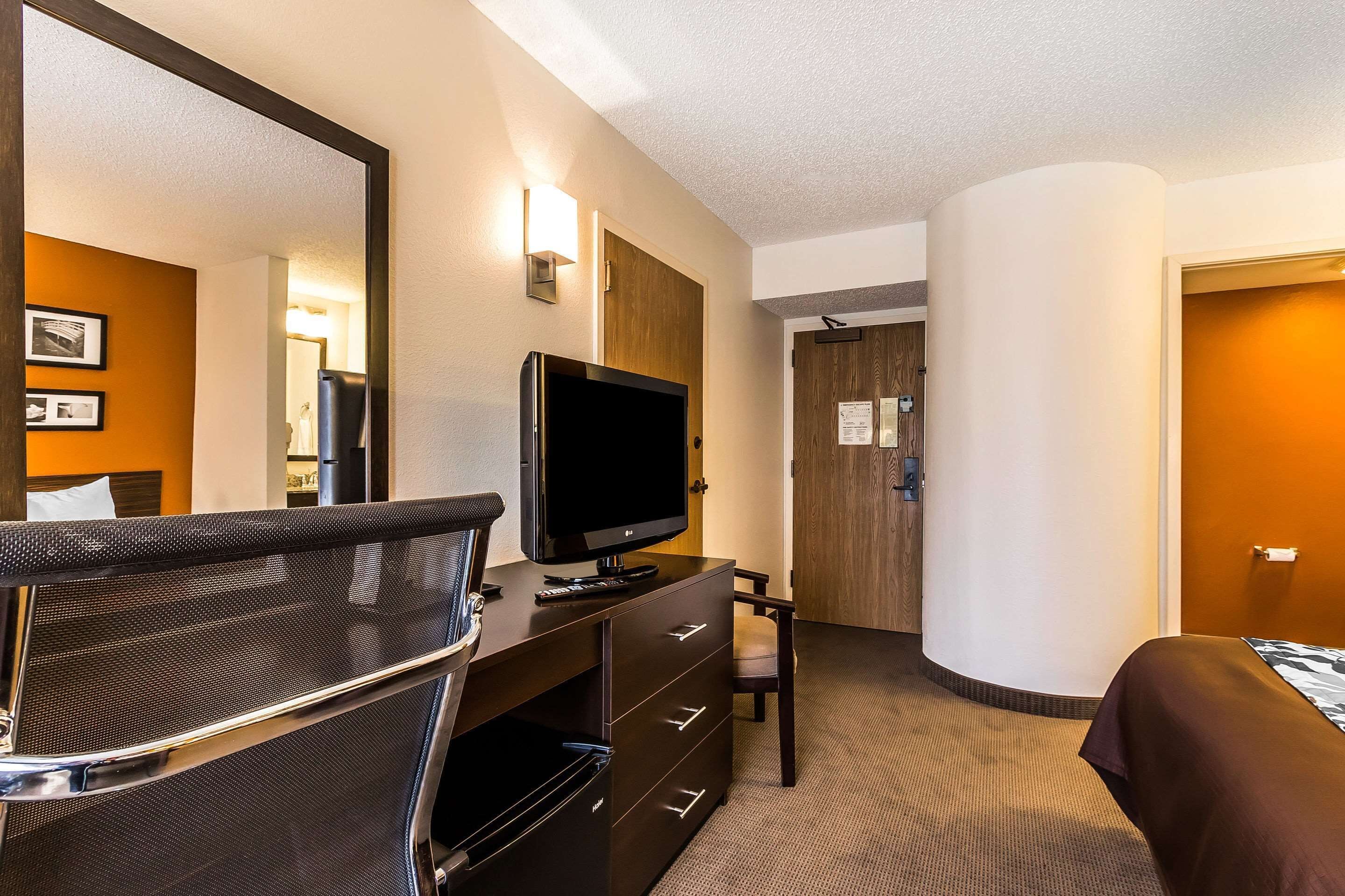 A hotel room with a bed, a desk with a television, a chair, and a large mirror.