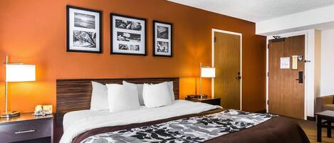 A hotel room with a bed, a nightstand, a lamp, and a door.