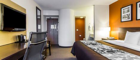 Habitación de hotel con cama, escritorio, silla, televisor y puerta que da a otra habitación.