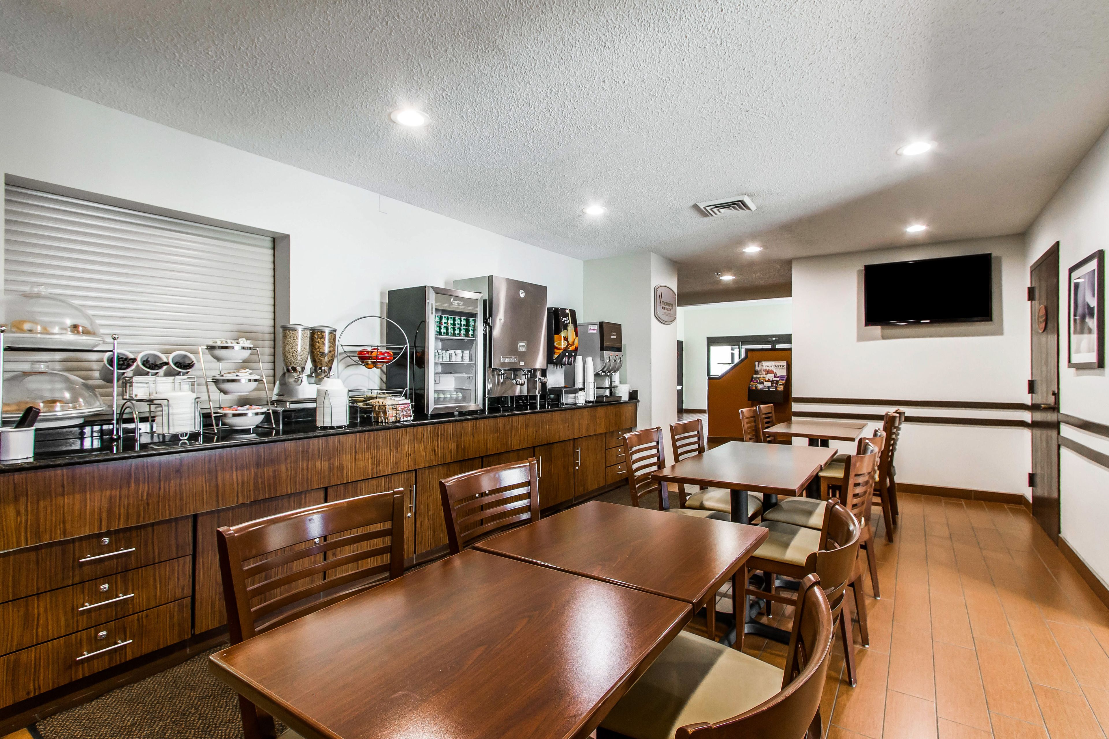 A restaurant with wooden tables and chairs, a kitchen area with appliances, and a television mounted on the wall.