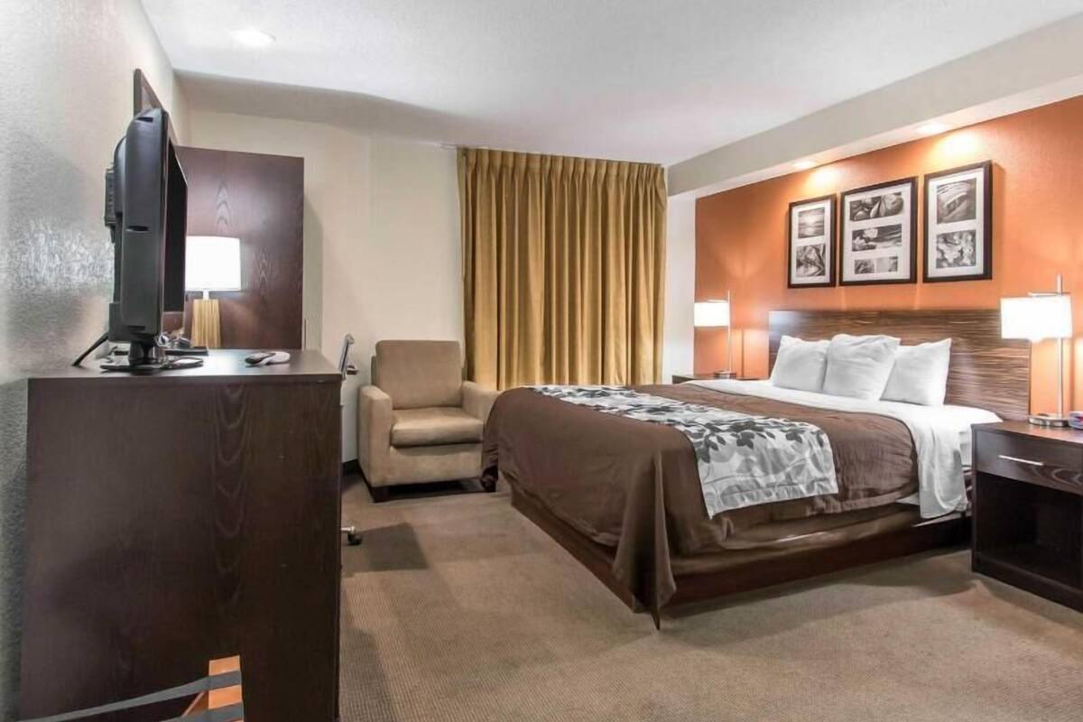 A hotel room with a bed, a desk, a chair, a television, and a wall with framed pictures.