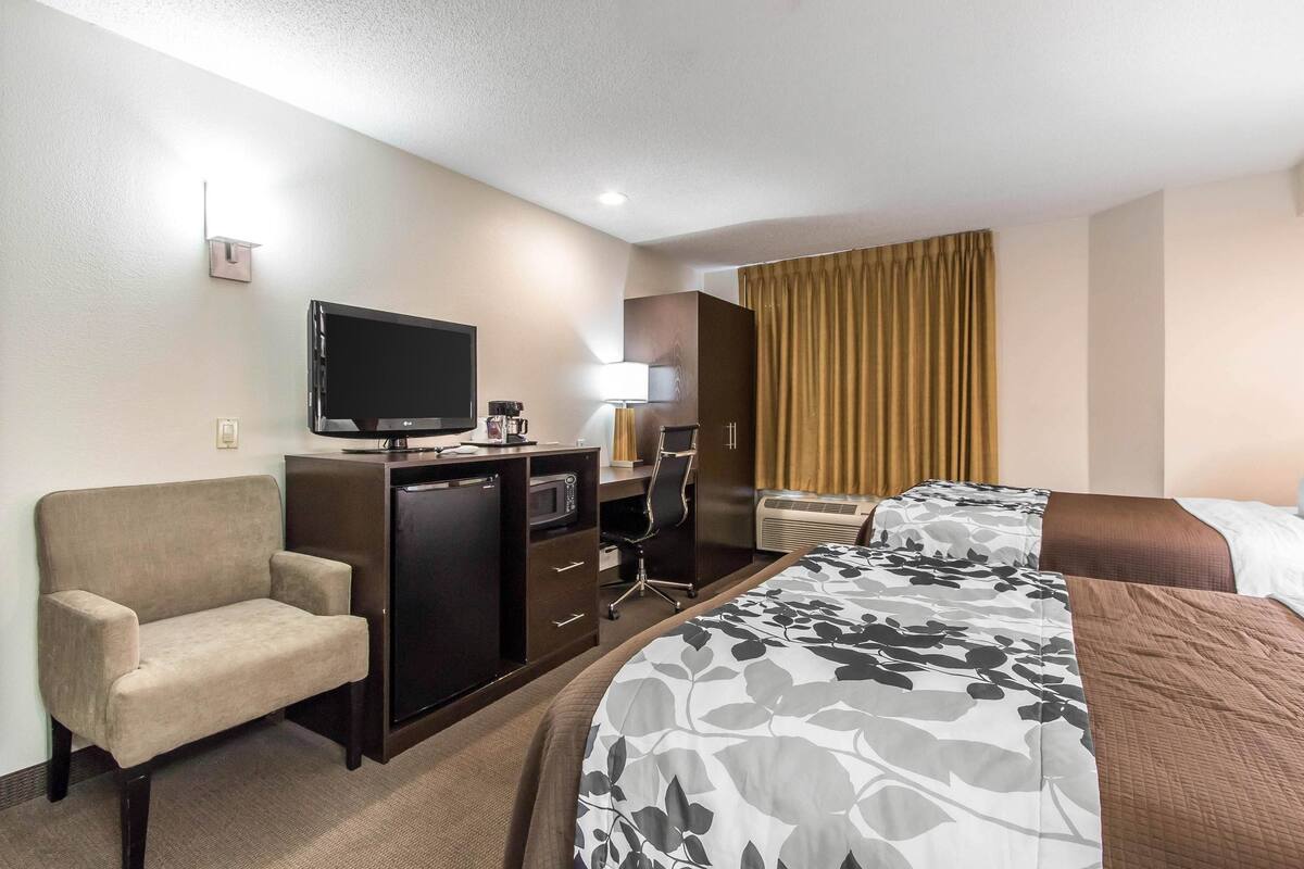 A hotel room with a bed, a desk, a chair, a television, and a window with curtains.