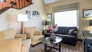 Quarto de hotel com sofá, duas poltronas, uma mesa de centro com um vaso, abajur e quadros nas paredes.