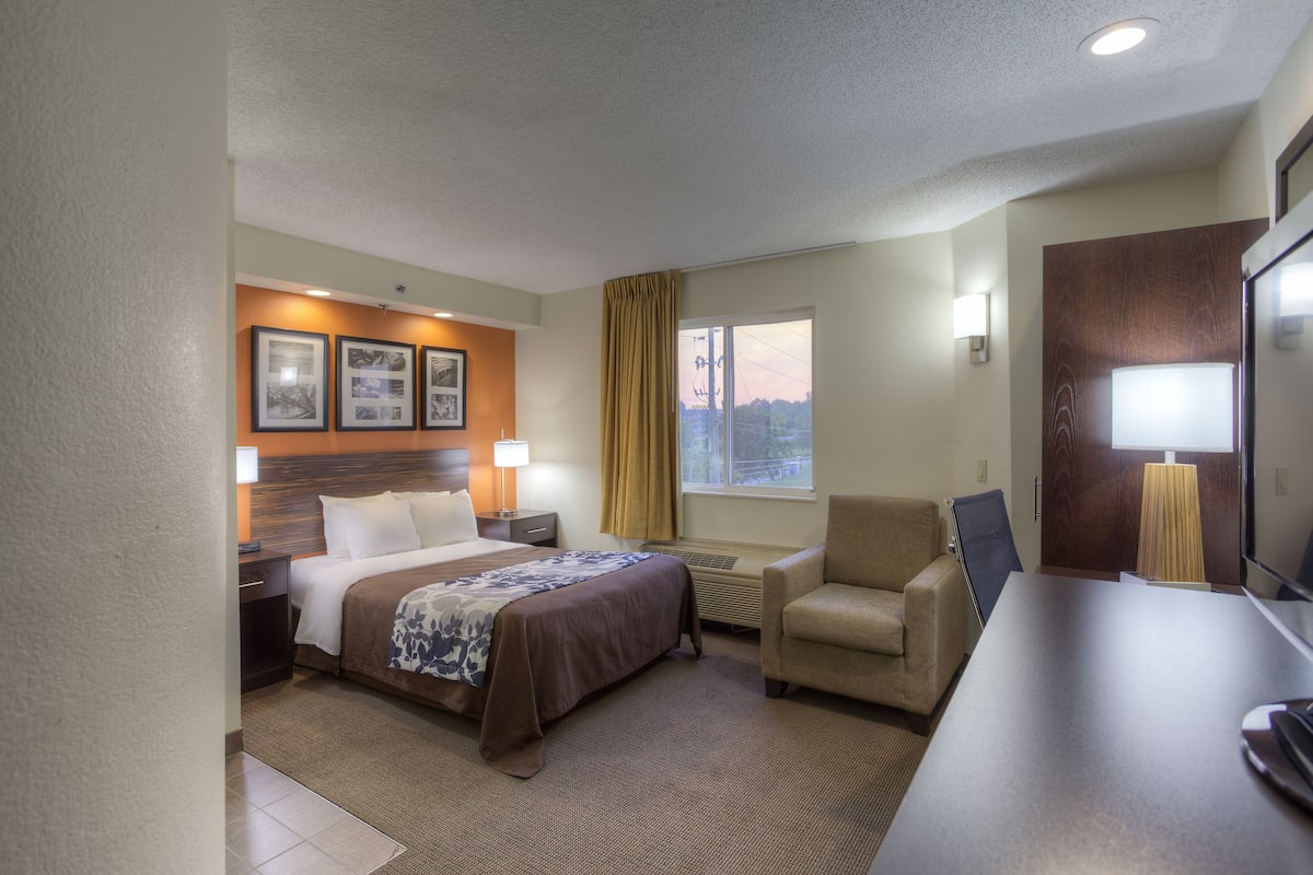 A hotel room with a bed, a desk, a chair, a TV, and a window with curtains.