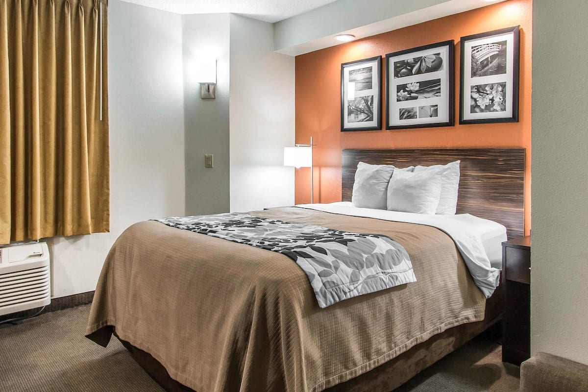 A hotel room with a bed, a nightstand, a lamp, and framed pictures on the wall.