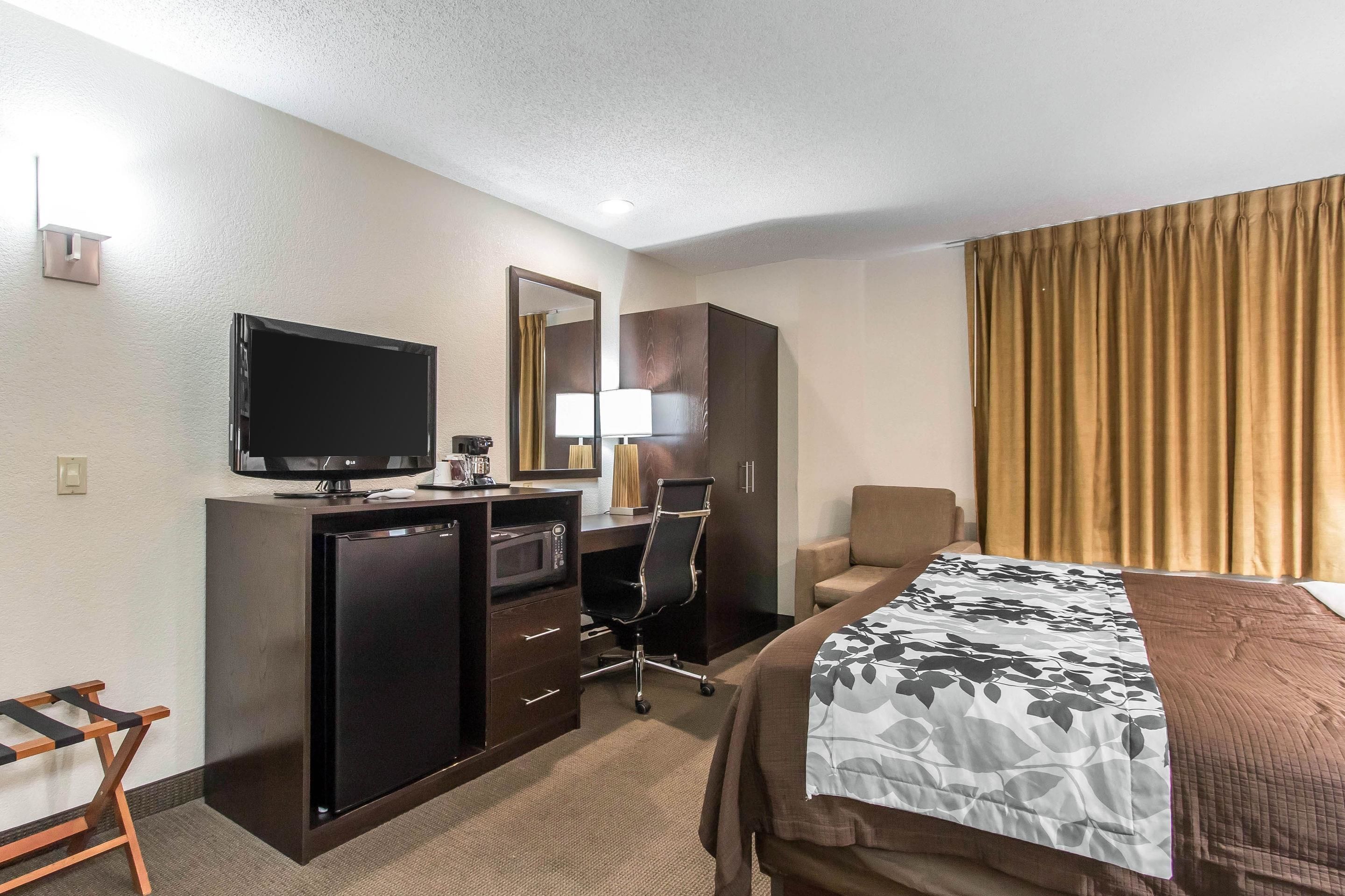 A hotel room with a bed, a desk with a computer, a television, and a minibar.