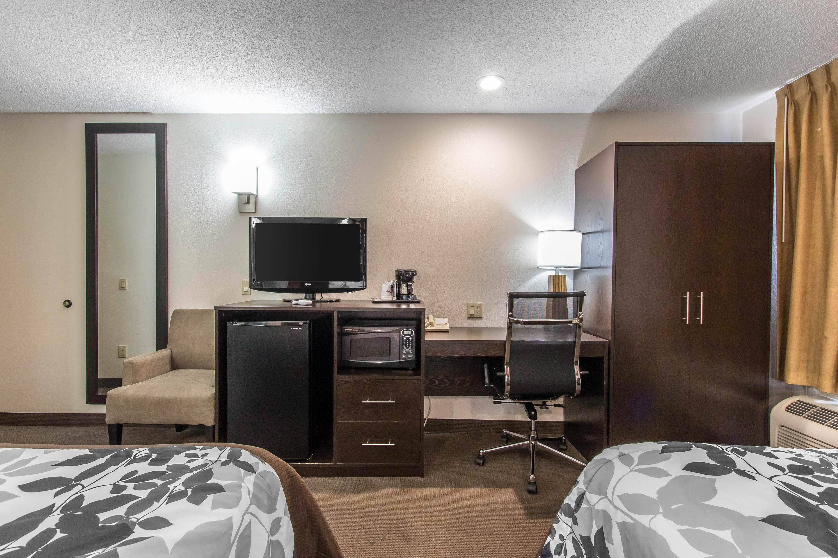 A hotel room with two beds, a desk with a computer, a microwave, a TV, a chair, and a wardrobe.