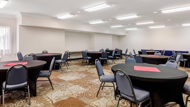 Un salón de conferencias con varias mesas y sillas, paredes blancas y una alfombra estampada.