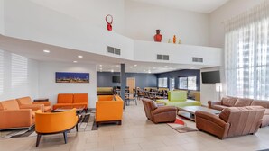 A spacious lobby with multiple seating areas, a high ceiling, and a cityscape painting. - Quality Inn & Suites Denver Airport - Gateway Park (Aurora)