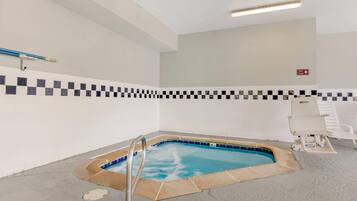 A small indoor pool with a checkered tile border, a spa timer sign, and a white lounge chair.