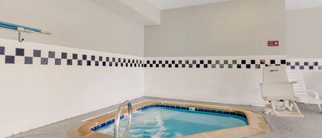 Una pequeña piscina interior con un borde de azulejos a cuadros, un cartel de temporizador de spa y una silla de descanso blanca.