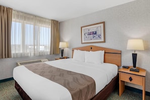 A hotel room with a large bed, two bedside tables with lamps, a window with curtains, a wall-mounted picture, and a carpeted floor. - Quality Inn & Suites Denver Airport - Gateway Park (Aurora)