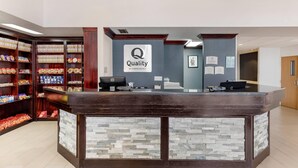 A hotel reception desk with a stone facade, a sign reading "Quality by Choice Hotels," and shelves stocked with snacks and beverages. - Quality Inn & Suites Denver Airport - Gateway Park (Aurora)