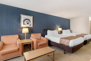 Una habitación de hotel con una cama, dos sillas, una mesita, una lámpara y un cuadro en la pared.