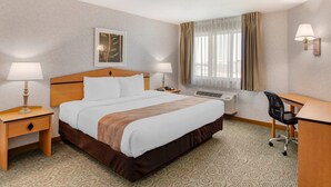 Habitación de hotel con una cama grande, dos mesitas de noche con lámparas, un escritorio con silla y una ventana con cortinas.
