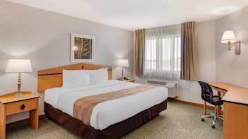 A hotel room with a large bed, two bedside tables with lamps, a desk with a chair, and a window with curtains.