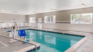 An indoor swimming pool with clear water, surrounded by white walls and a tiled floor.