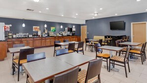 A dining area with tables and chairs, a kitchen area with appliances, and a television mounted on the wall.
