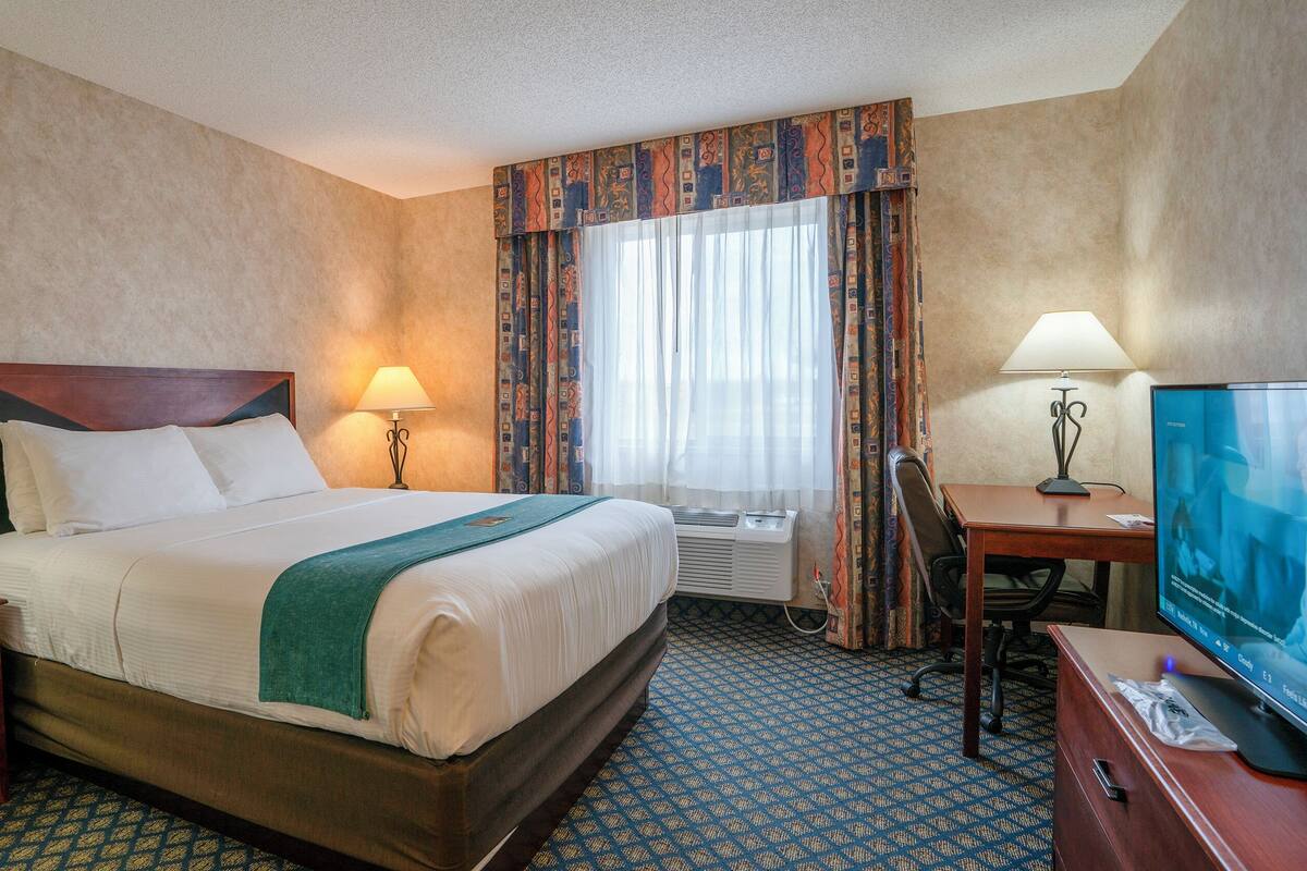 Habitación de hotel con cama, mesitas de noche, un escritorio con silla, televisor y ventana con cortinas.