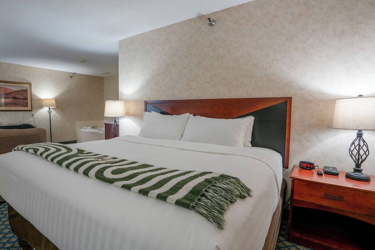 Una habitación de hotel con cama, escritorio, silla, lámpara y reloj.