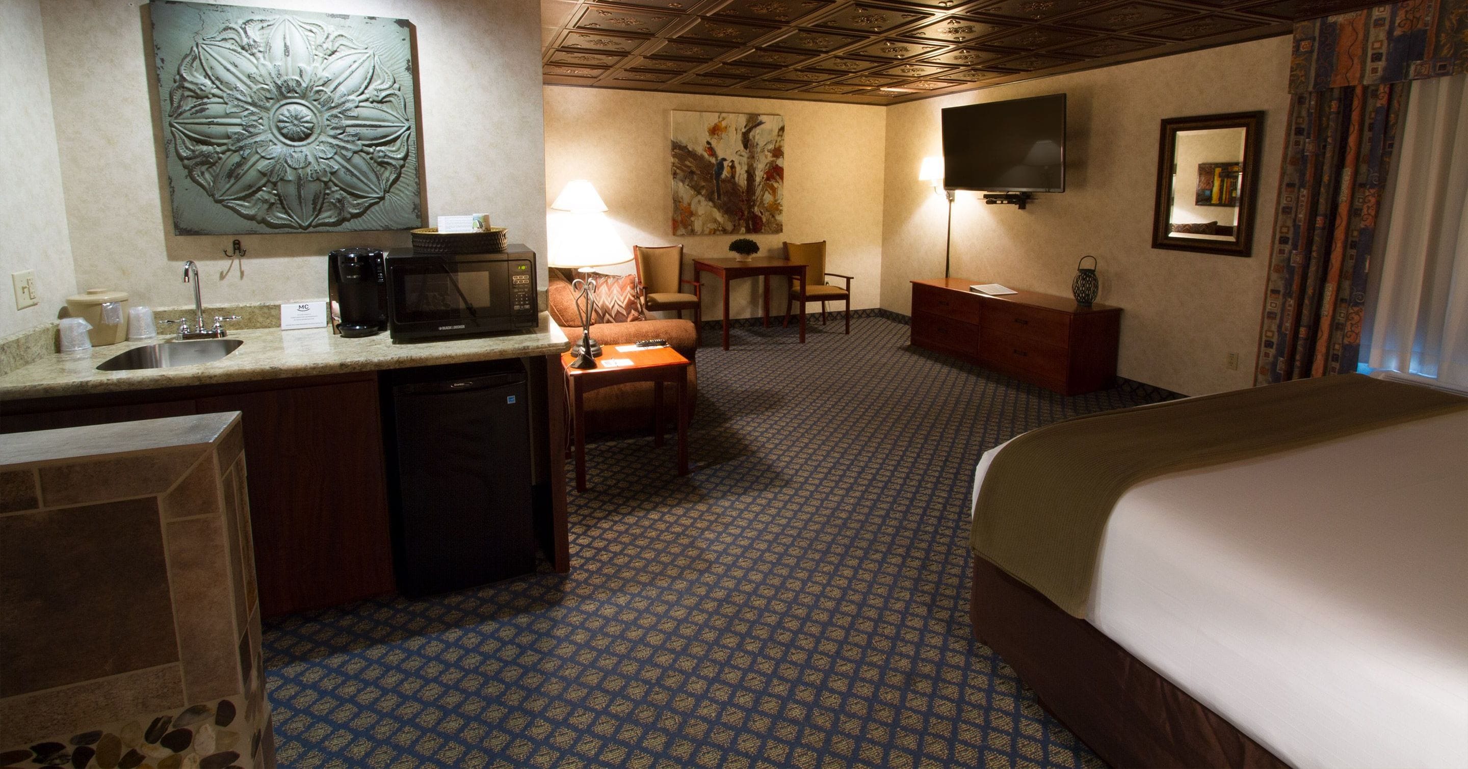 Habitación de hotel con cama, escritorio, silla, televisión, microondas y lavabo.