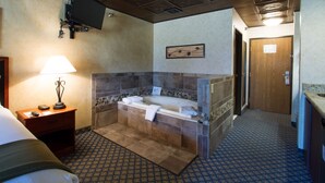 Habitación de hotel con una cama grande, un área de descanso con una lámpara, un baño con bañera y ducha.