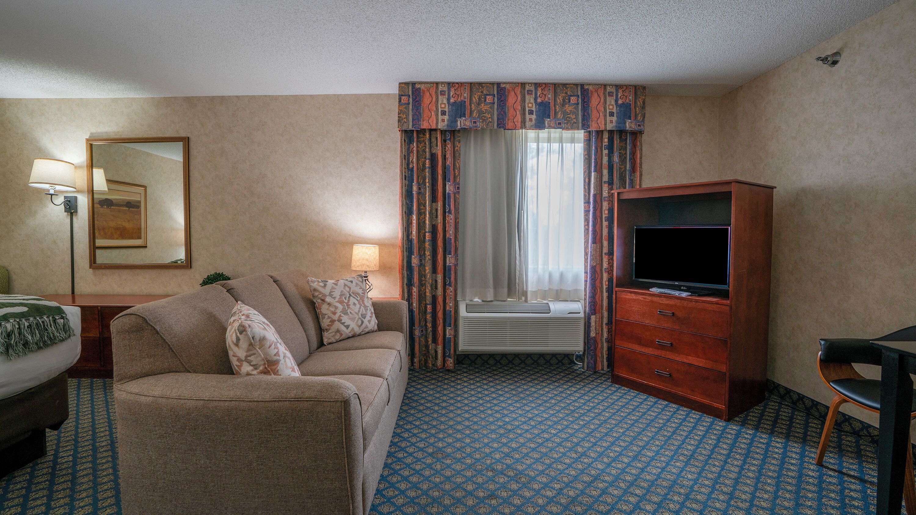 A hotel room with a sofa, a TV stand, a desk, and a window with curtains.