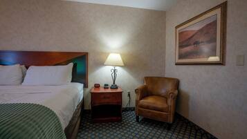 Habitación de hotel con cama, mesita de noche con lámpara, una silla y un cuadro en la pared.