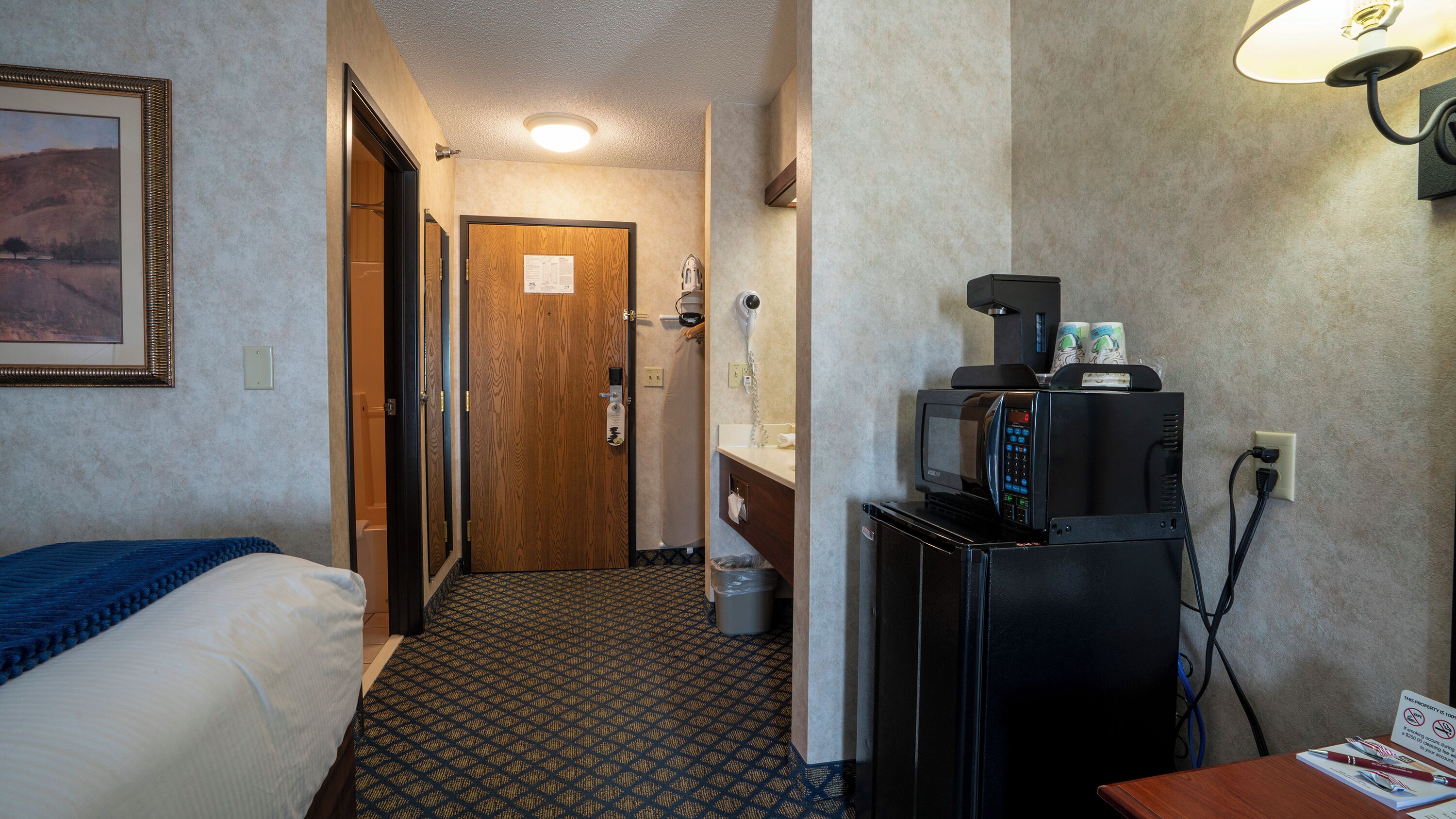 Une chambre d’hôtel équipée d’un lit, d’un bureau avec un micro-ondes, d’un sèche-cheveux et d’une poubelle.