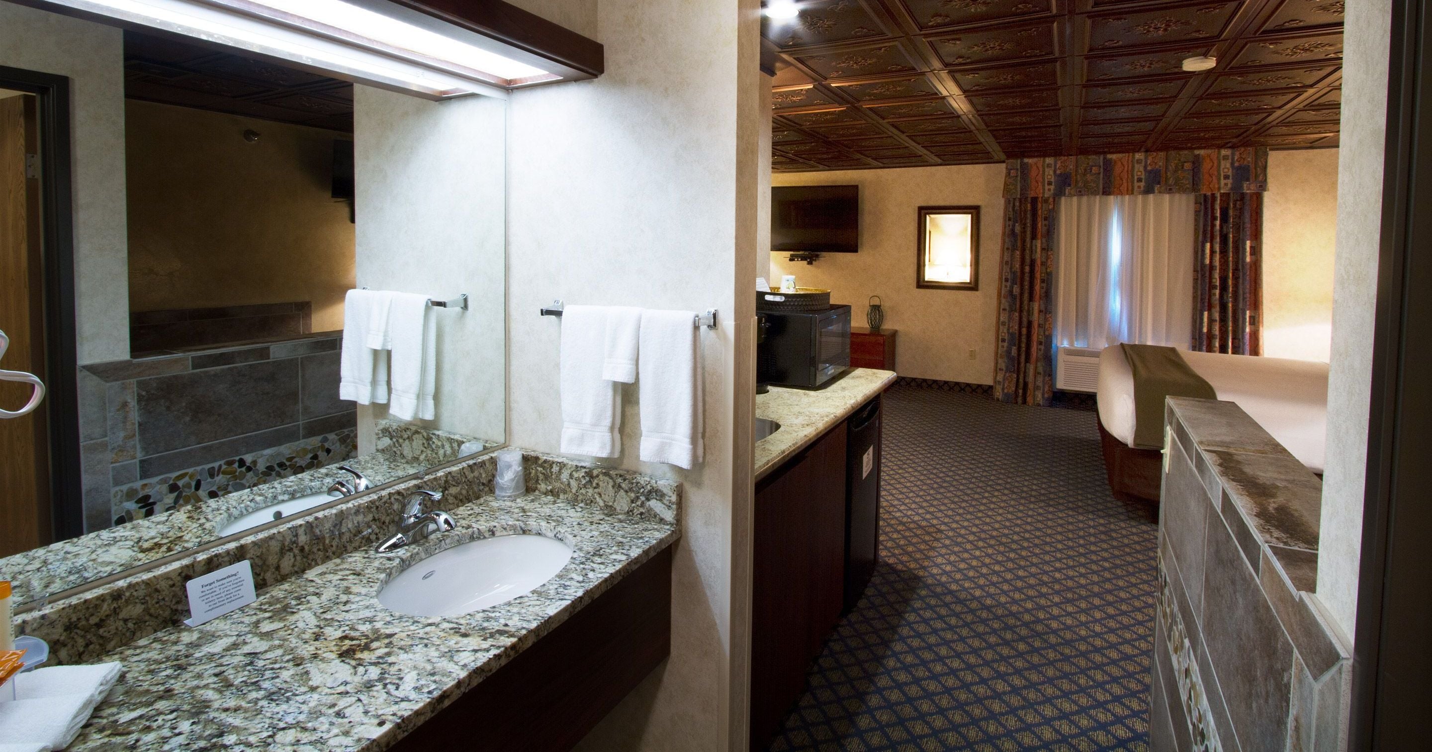 A bathroom with a granite sink, two mirrors, a television, and a patterned floor.