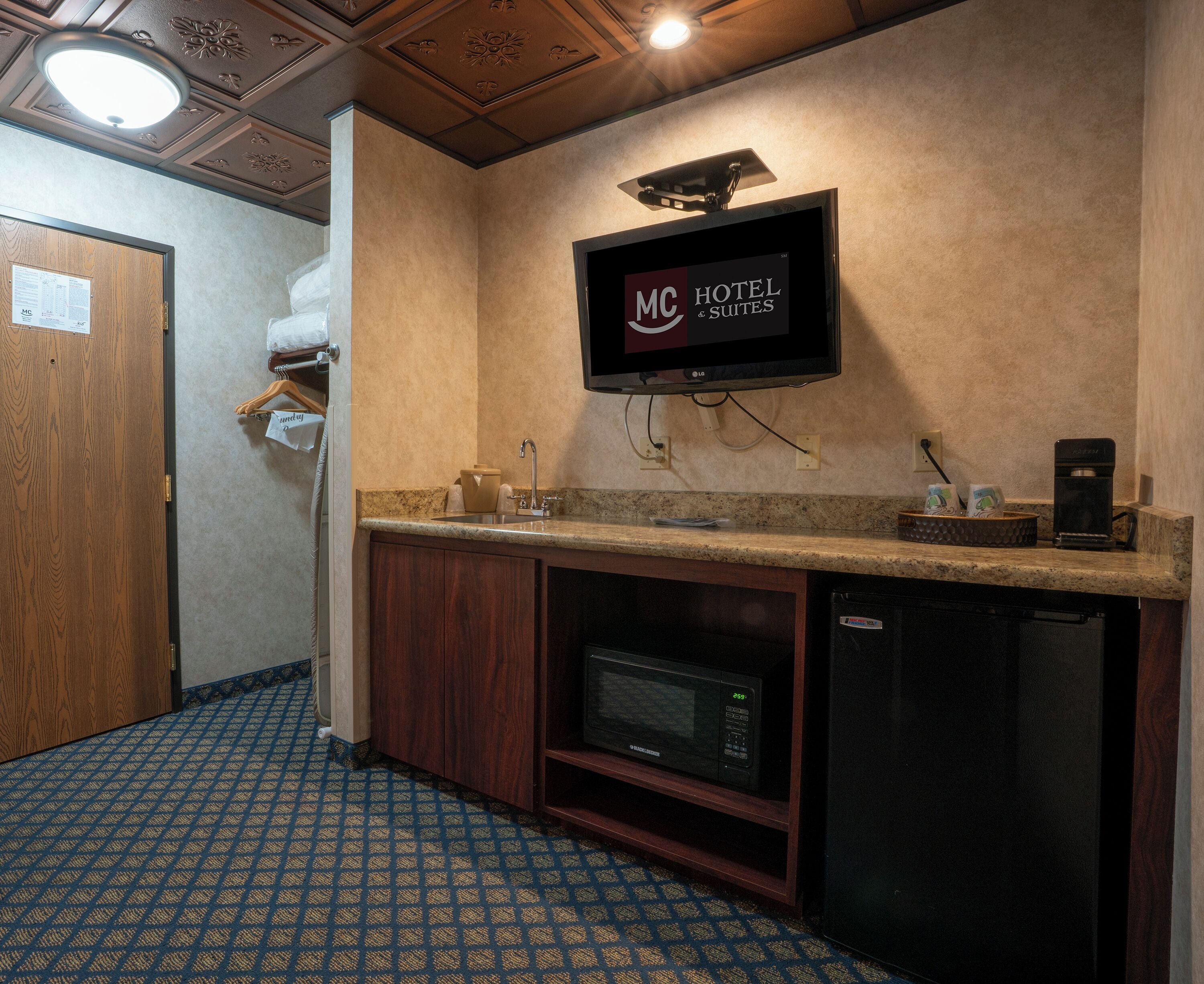 A hotel kitchenette with a microwave, coffee maker, and a TV displaying "HOTEL & SUITES".