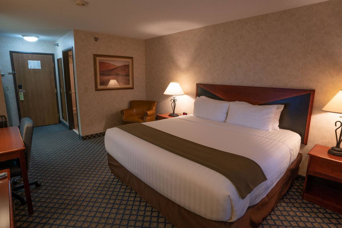 Una habitación de hotel con una cama grande, un escritorio, una silla y una mesita de noche con una lámpara.