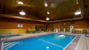 Una piscina interior con techo de madera, suelo de baldosas y algunas sillas y mesas alrededor de la zona de la piscina.