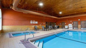 Una piscina interior con techo de madera, suelo de baldosas y una zona de estar con sillas y mesas.