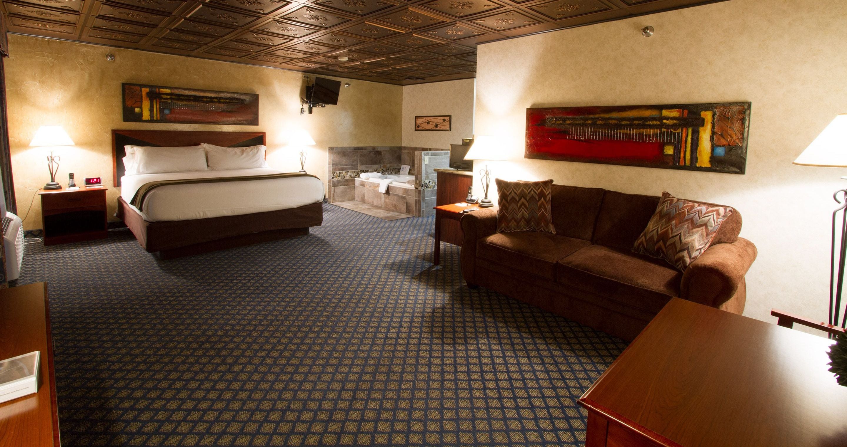 A hotel room with a bed, a sofa, a desk, a TV, and a painting on the wall.