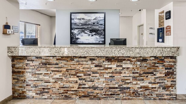 A reception area with a granite counter, a stone mosaic wall, and a large landscape painting above the counter. - Baymont by Wyndham Loveland/Fort Collins Area (Loveland)