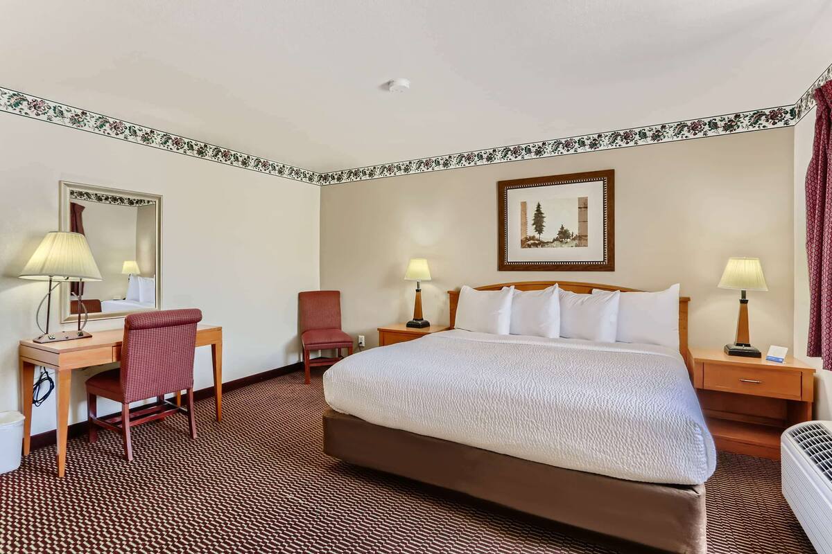 A hotel room with a large bed, two bedside tables with lamps, a desk with a chair, a mirror, and a framed picture on the wall.