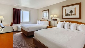 A hotel room with two beds, a desk, a chair, a window with curtains, a wall-mounted mirror, and a framed picture. - Baymont by Wyndham Loveland/Fort Collins Area (Loveland)