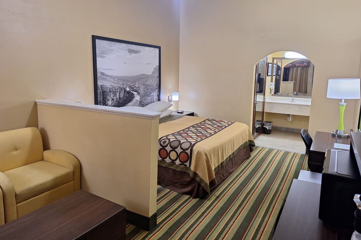 A hotel room with a bed, a sofa, a desk, a mirror, and a ceiling fan.
