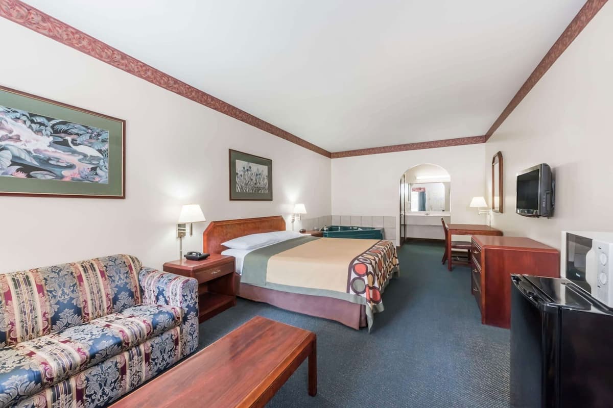 A hotel room with a bed, a sofa, a desk, a TV, a mirror, and a painting on the wall.