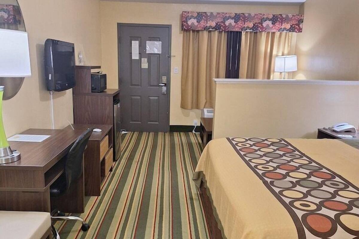 A hotel room with a bed, desk, chair, television, and a door.