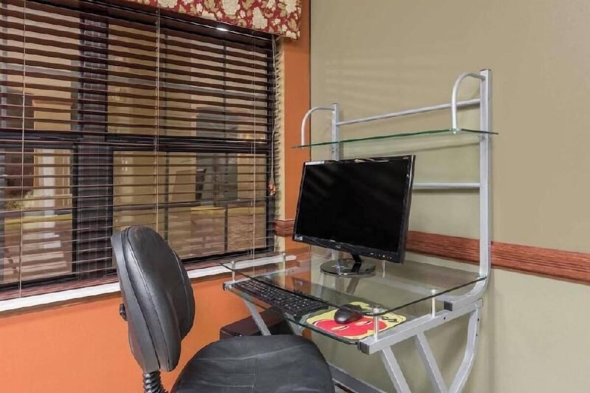 A computer desk with a monitor, keyboard, and mouse, a chair, and a window with blinds.