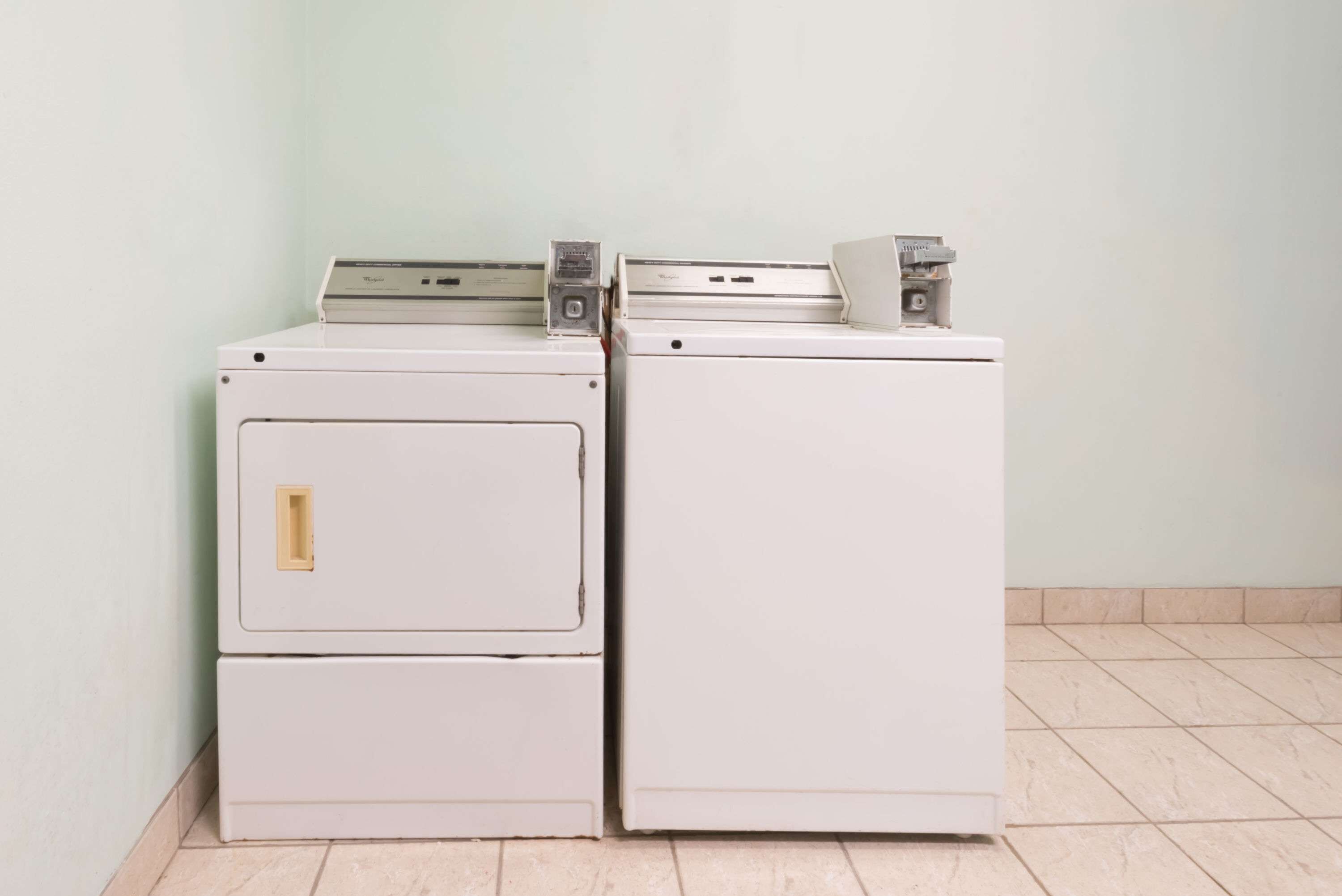 Two stacked washing machines in a corner with a plain wall and tiled floor.