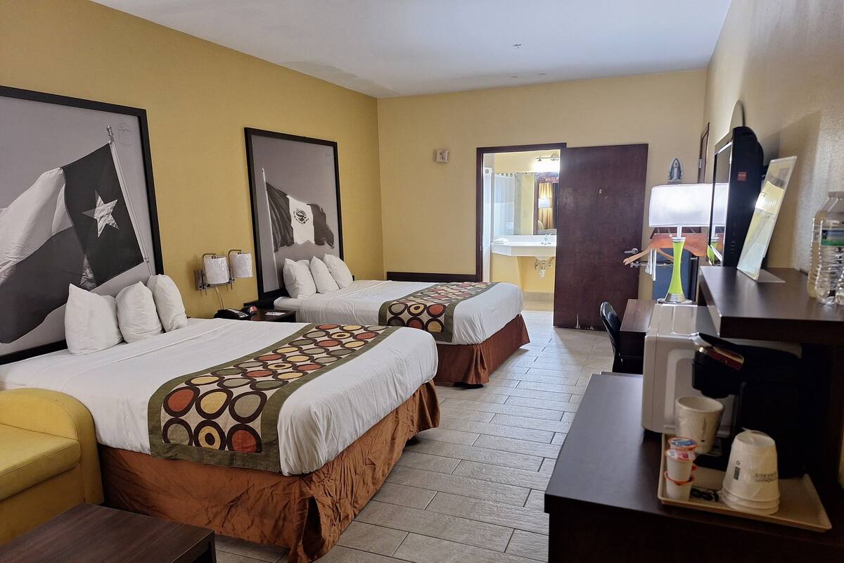 A hotel room with two beds, a desk with a coffee machine, and a bathroom visible through an open door.
