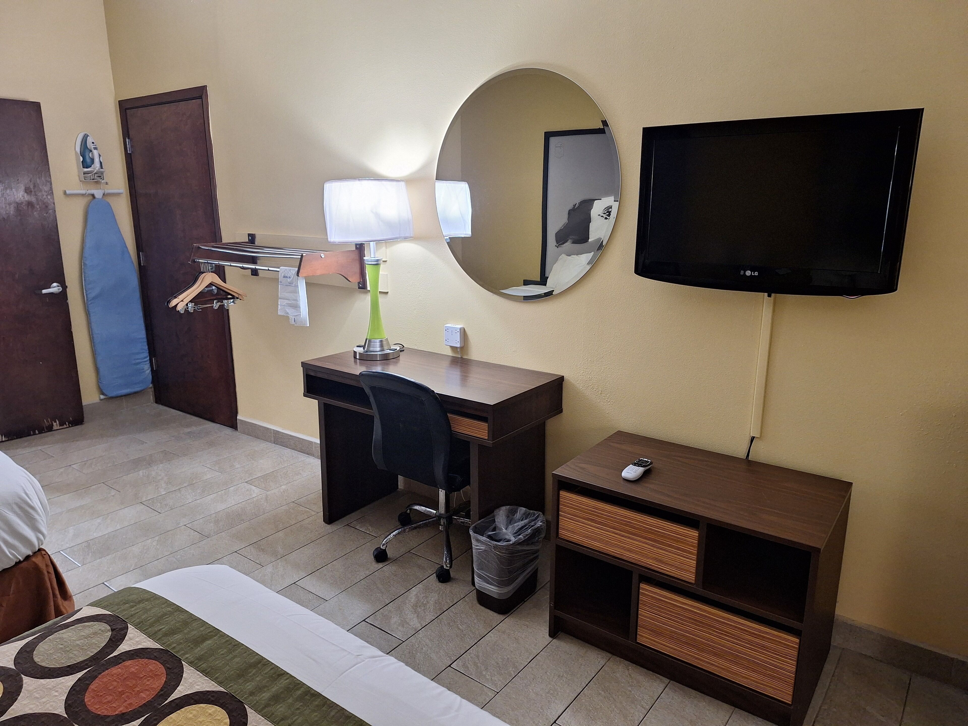A hotel room with a bed, desk, chair, TV, and a small table with a remote control.
