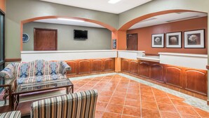 Un hall con un sofá, un sillón y un televisor montado en la pared.