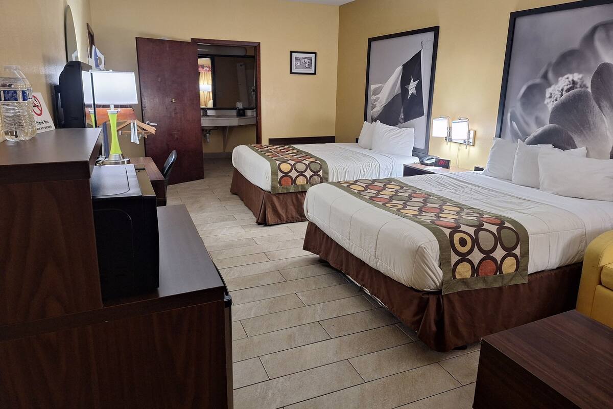 A hotel room with two beds, a desk, a chair, a bathroom, and a large window.